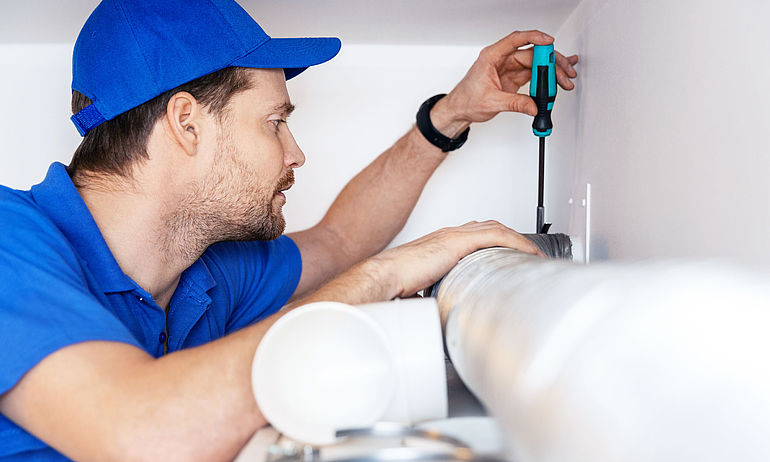 man with blue basecap and blue polo shirt working with screwdriver on ventilation system