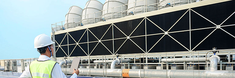 2-cooling towers Man with safety helmet and high-visibility vest stands on the roof of a cooling tower