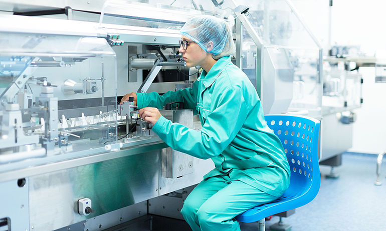 Lab technician in protective clothing sits on blue chair in clean room