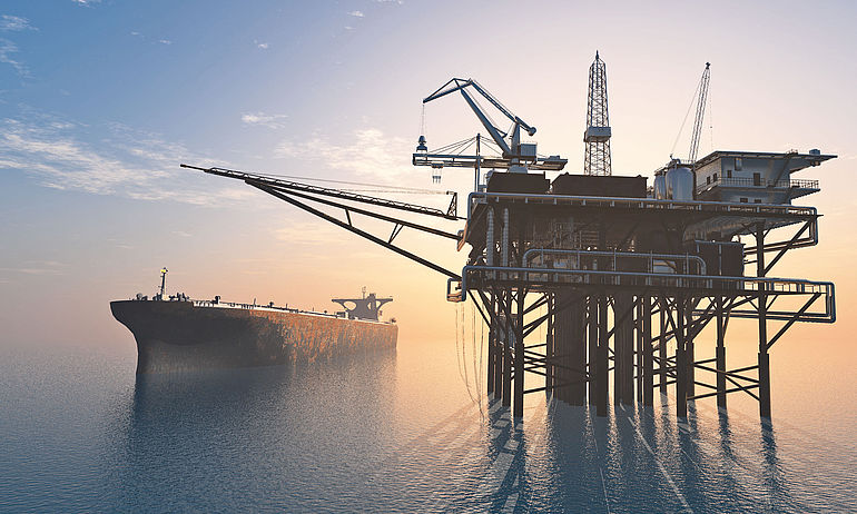 Oil tanker next to an oil rig at sea at sunset