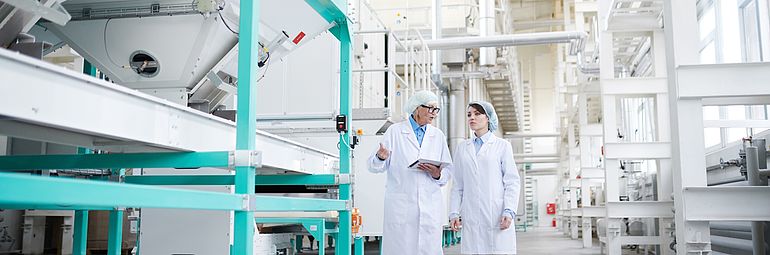 two people with work coat and hair net next to food production machine