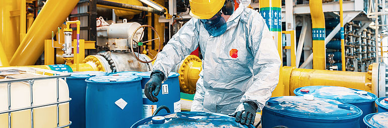 Person wearing protective clothing working on blue drums