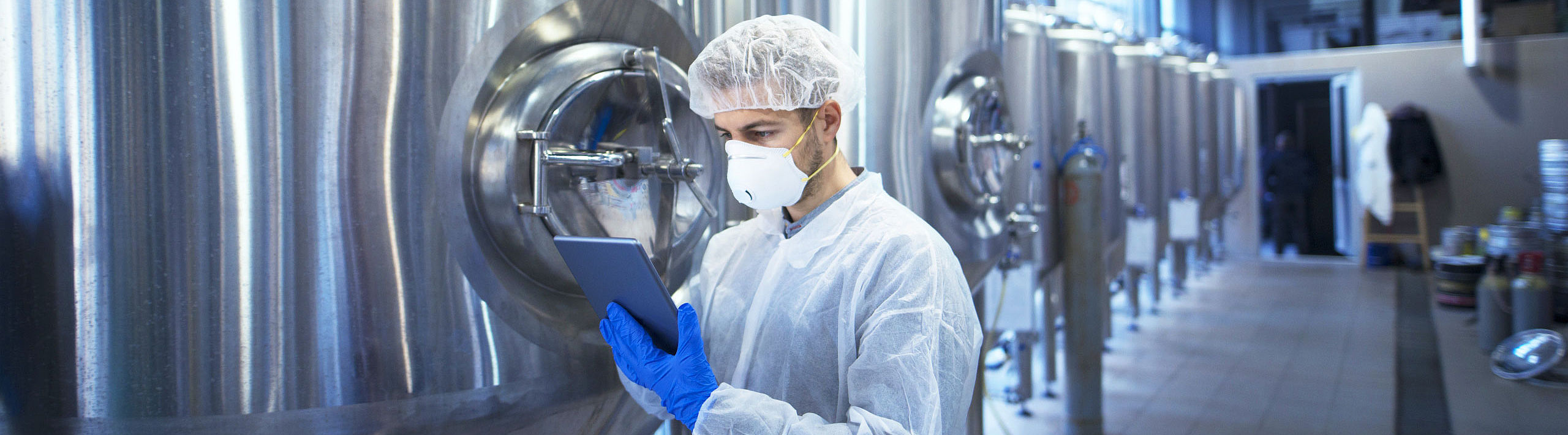 03-beverages man with tablet pc next to big metal tanks for beverage production