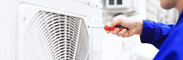 Man with blue work clothes and screwdriver on white fan grille