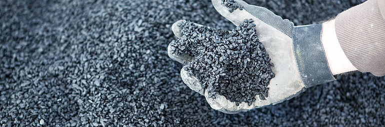 Hand in a glove gripping dark gray granules