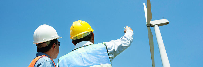two engineers with helmet and high visibly vest watching a wind turbine