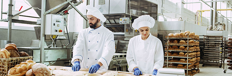 male and female baker with blue gloves form dough in industrial bakery
