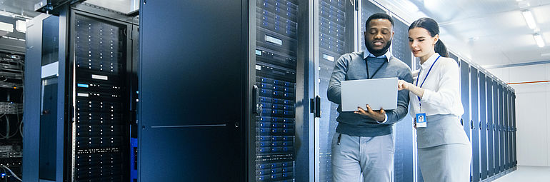 Man and woman with laptop in front of server cabinets