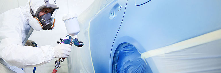 Person in protective clothing painting vehicle chassis blue