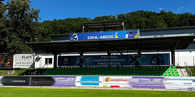 ZIEHL-ABEGG als Sponsor im Bereich Sport Tribüne mit ZIEHL-ABEGG Bannern hinter grünem Rasen